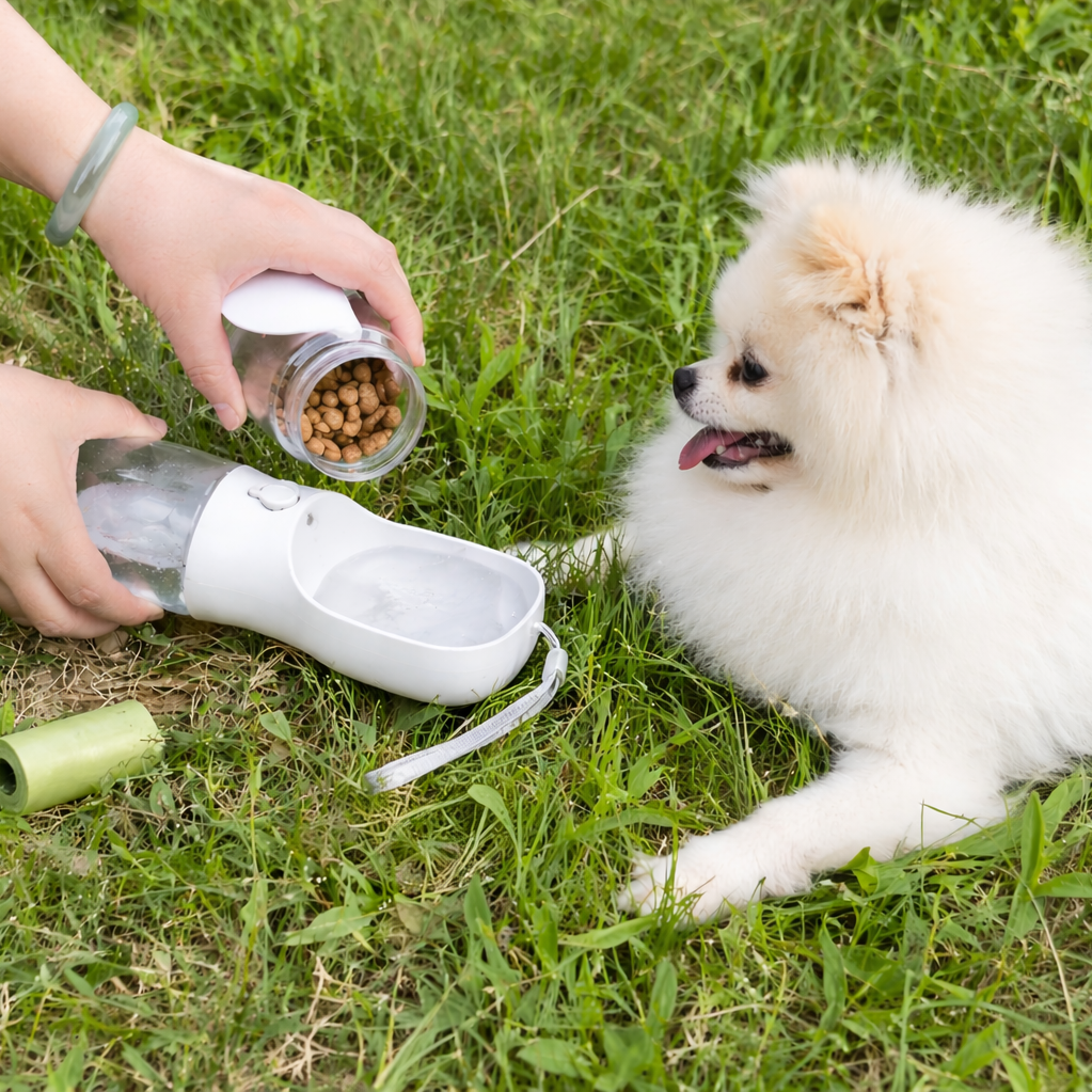 Person pouring dog food into a portable pet feeder next to a small white dog on grass.